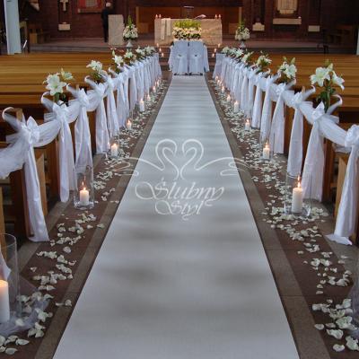 Wystrój kościoła na ślub - płatki żywych róż wzdłuż białego dywanu  i nastrojowe świeczki